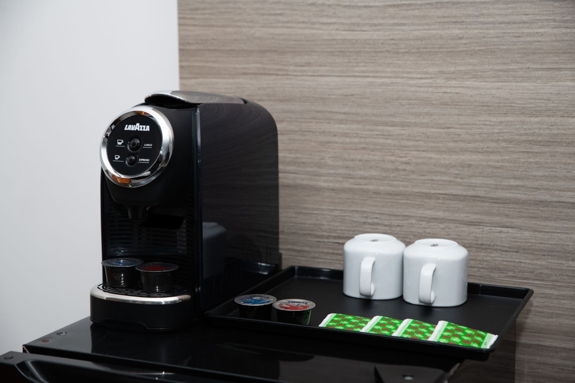 A mini espresso machine, a compact single-serve coffee maker, is the central focus, with coffee pods and cups arranged nearby for use.