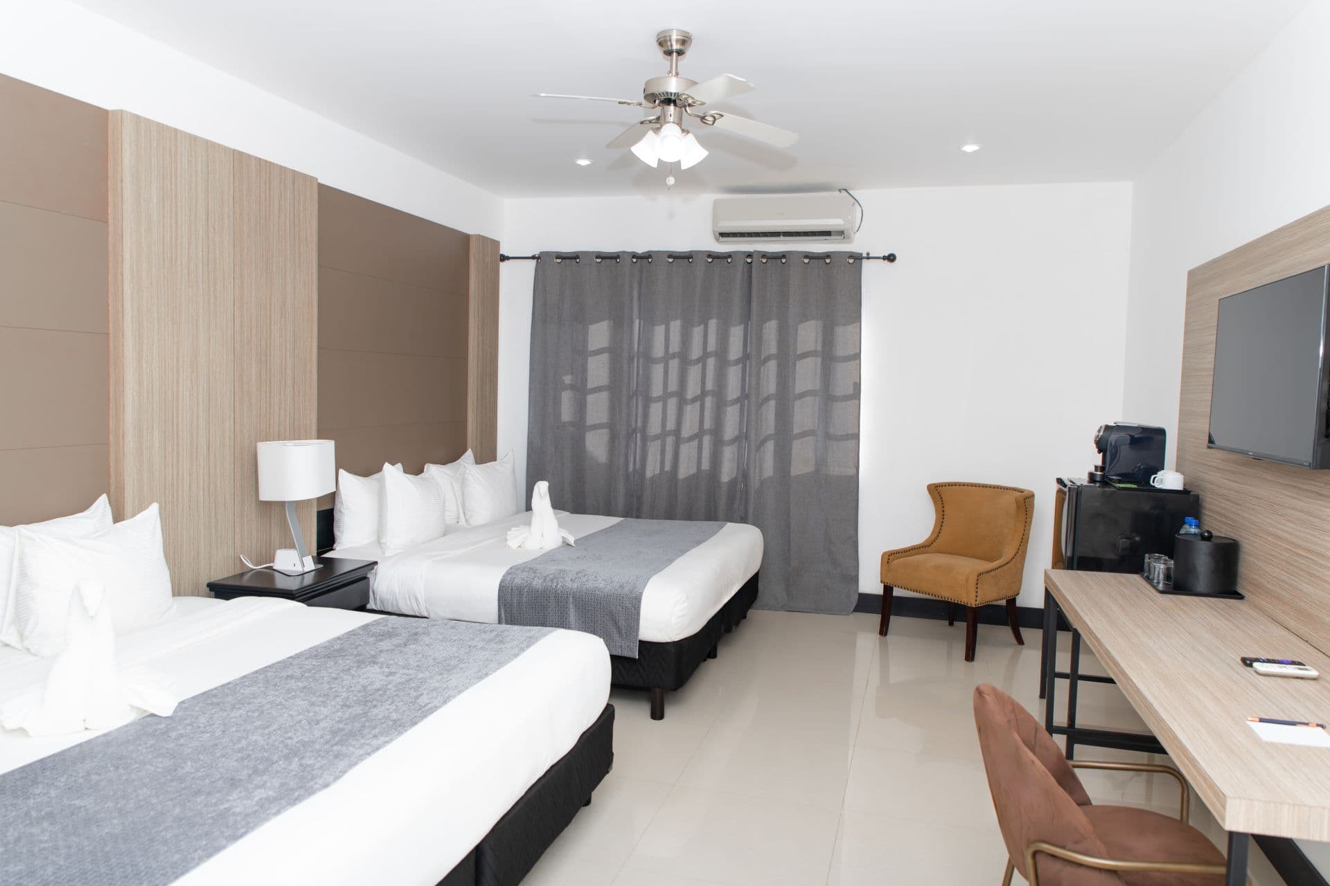 A hotel room with two beds, a desk area with a wall-mounted television and a coffee maker.