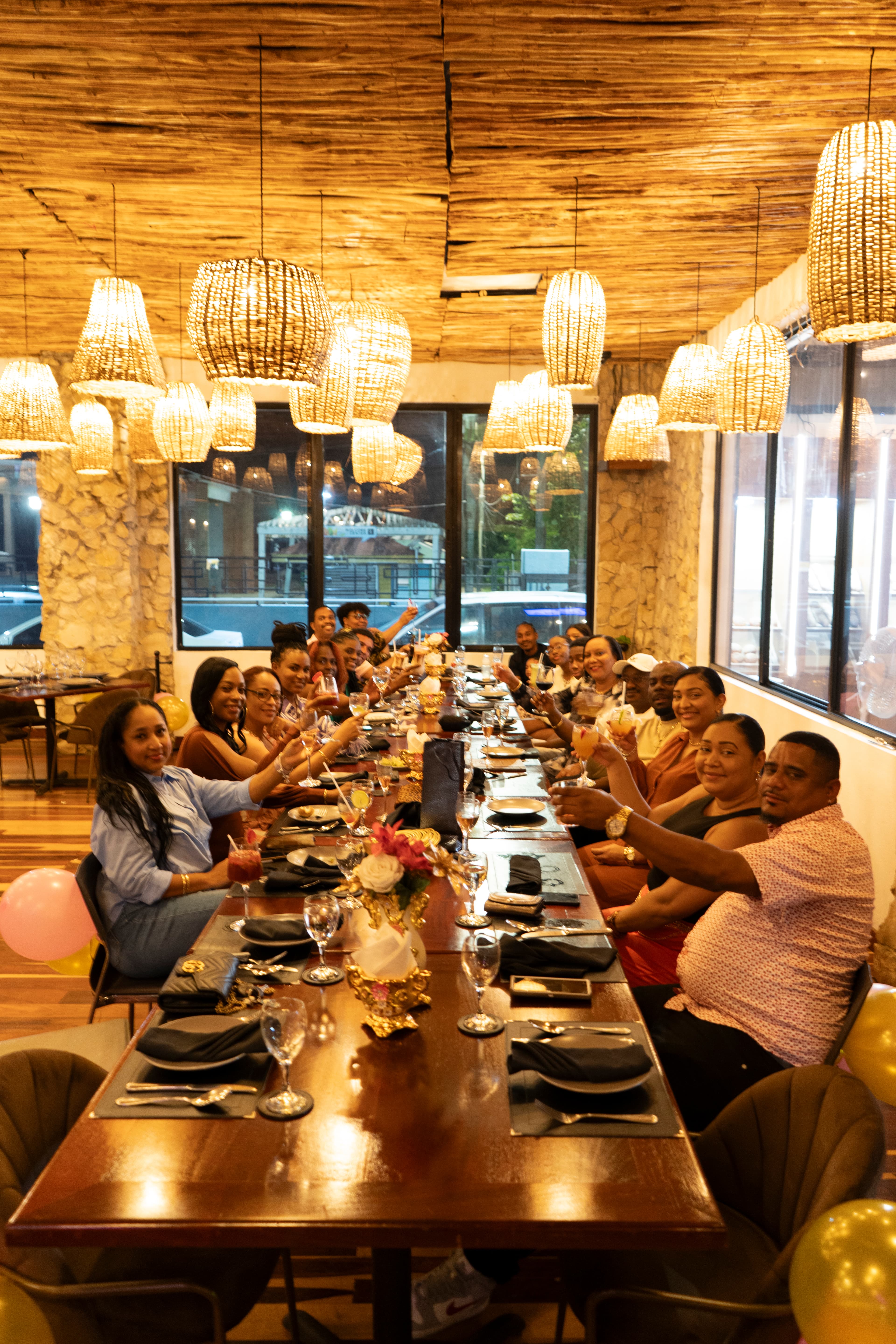 A group of people cheerfully toasting at a long dining table in a warmly lit restaurant.