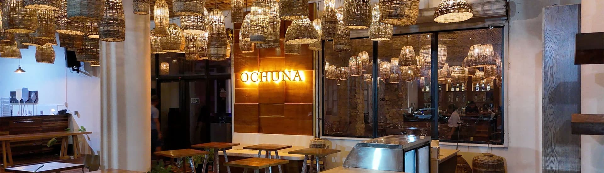 A cozy restaurant interior featuring hanging woven light fixtures and wooden tables.