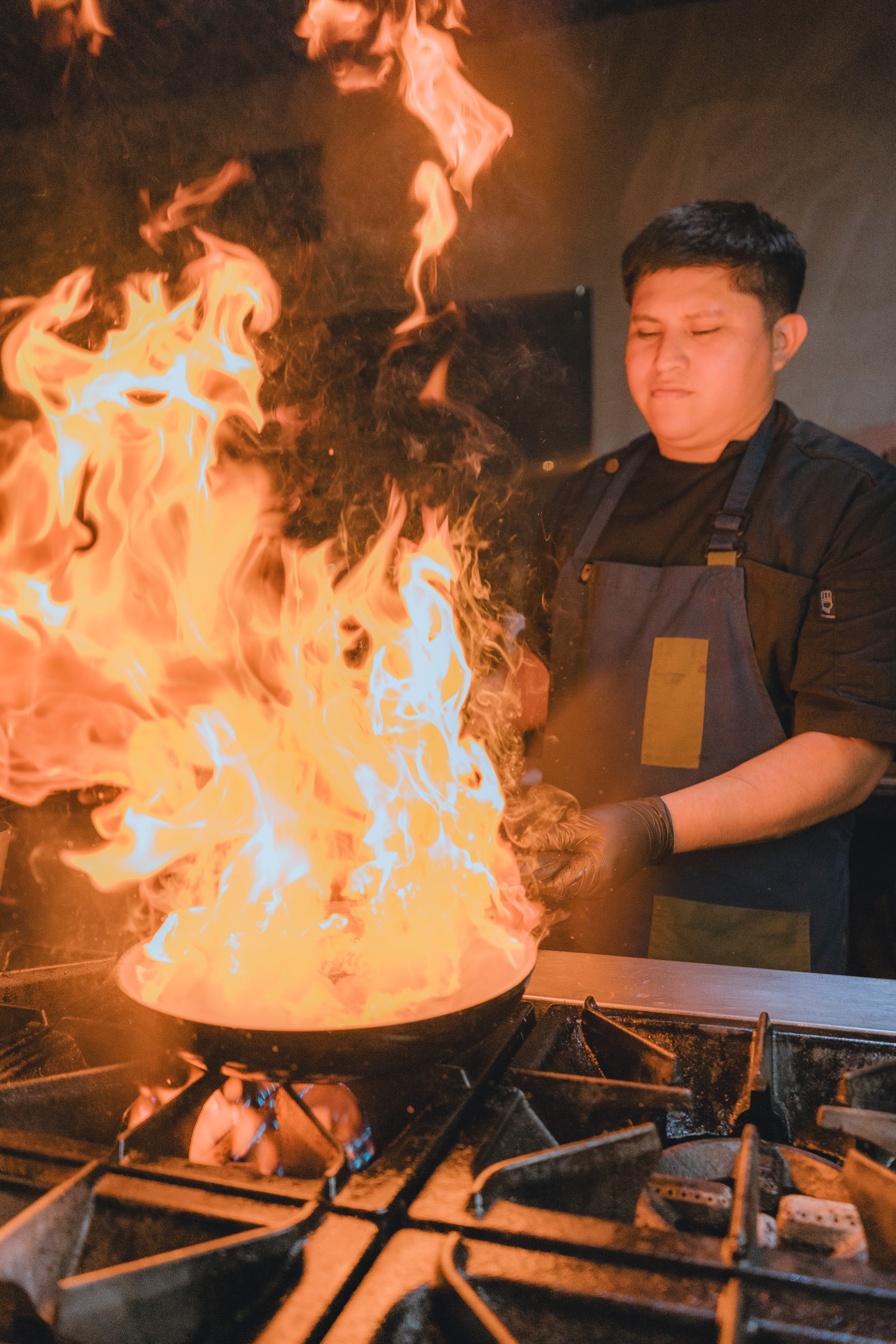 A chef skillfully cooks over a blazing fire in a professional kitchen.