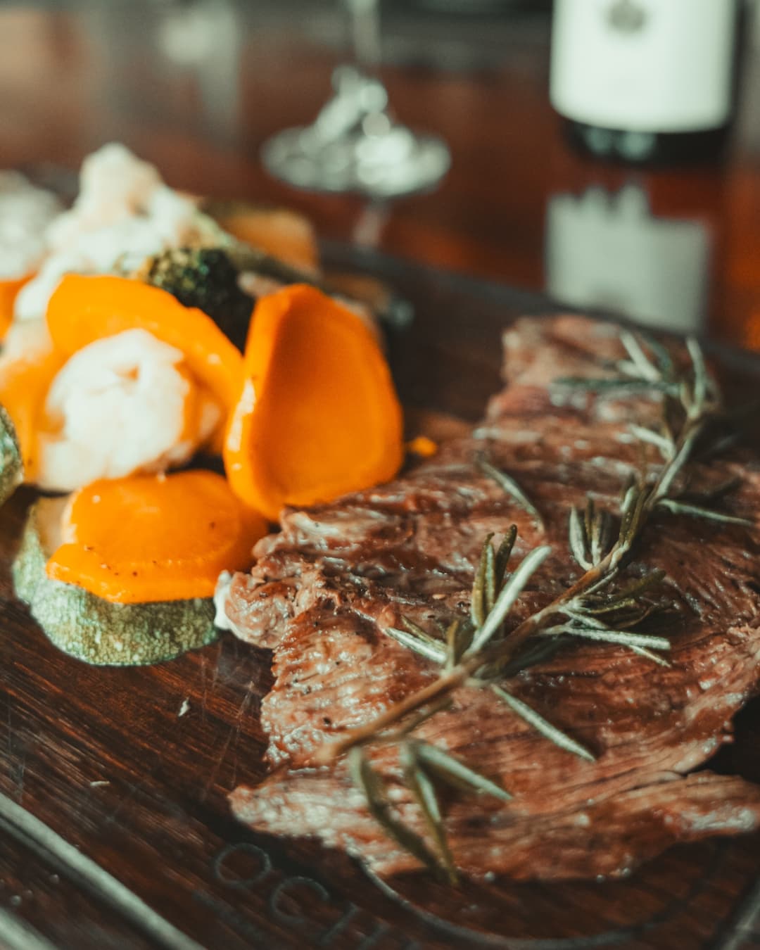 A plate of grilled steak garnished with rosemary, accompanied by colorful vegetables.