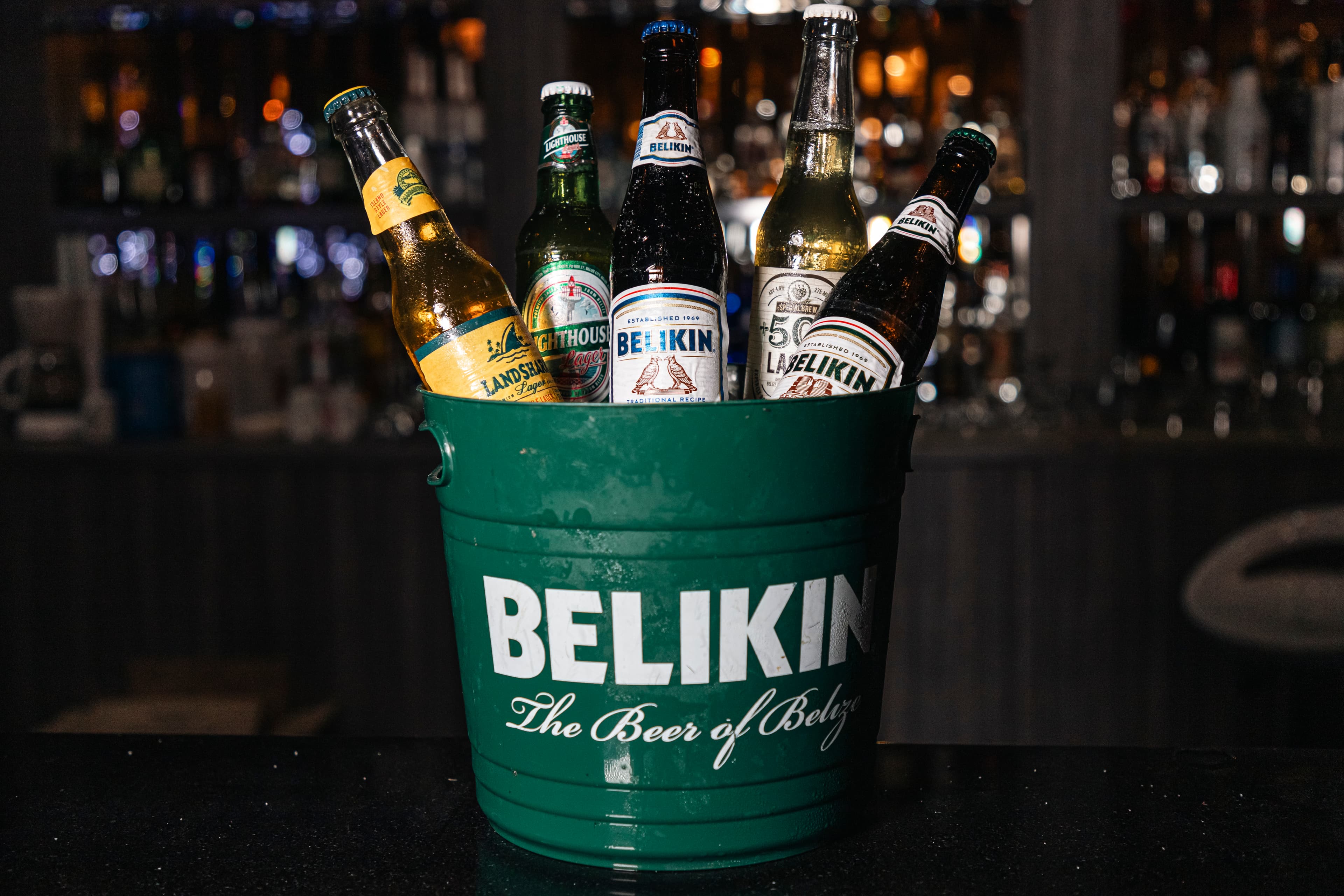 A green bucket filled with various beer bottles, prominently featuring "Belikin" branding.