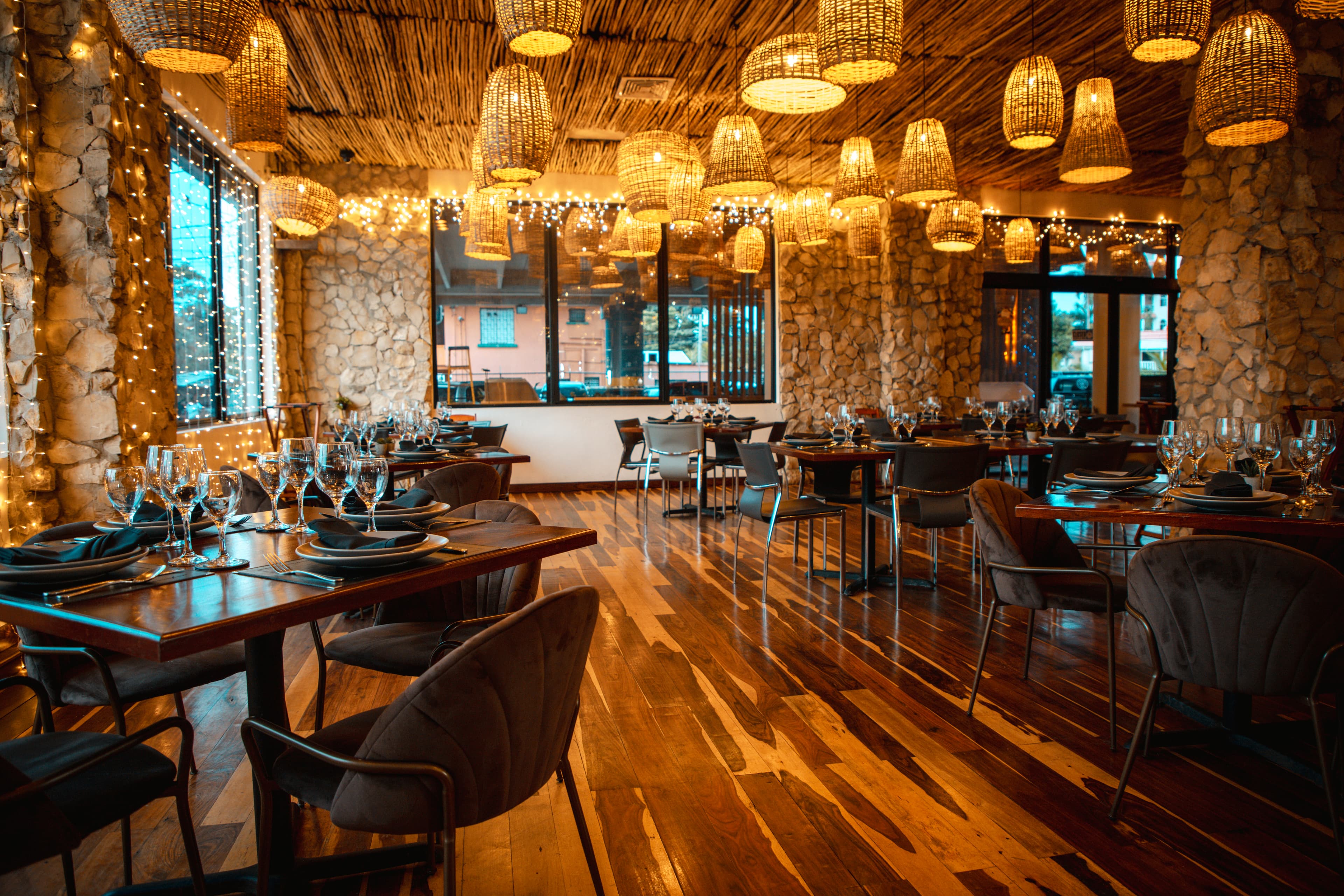 A cozy restaurant interior featuring wooden tables, elegant table settings, and warm hanging lights.