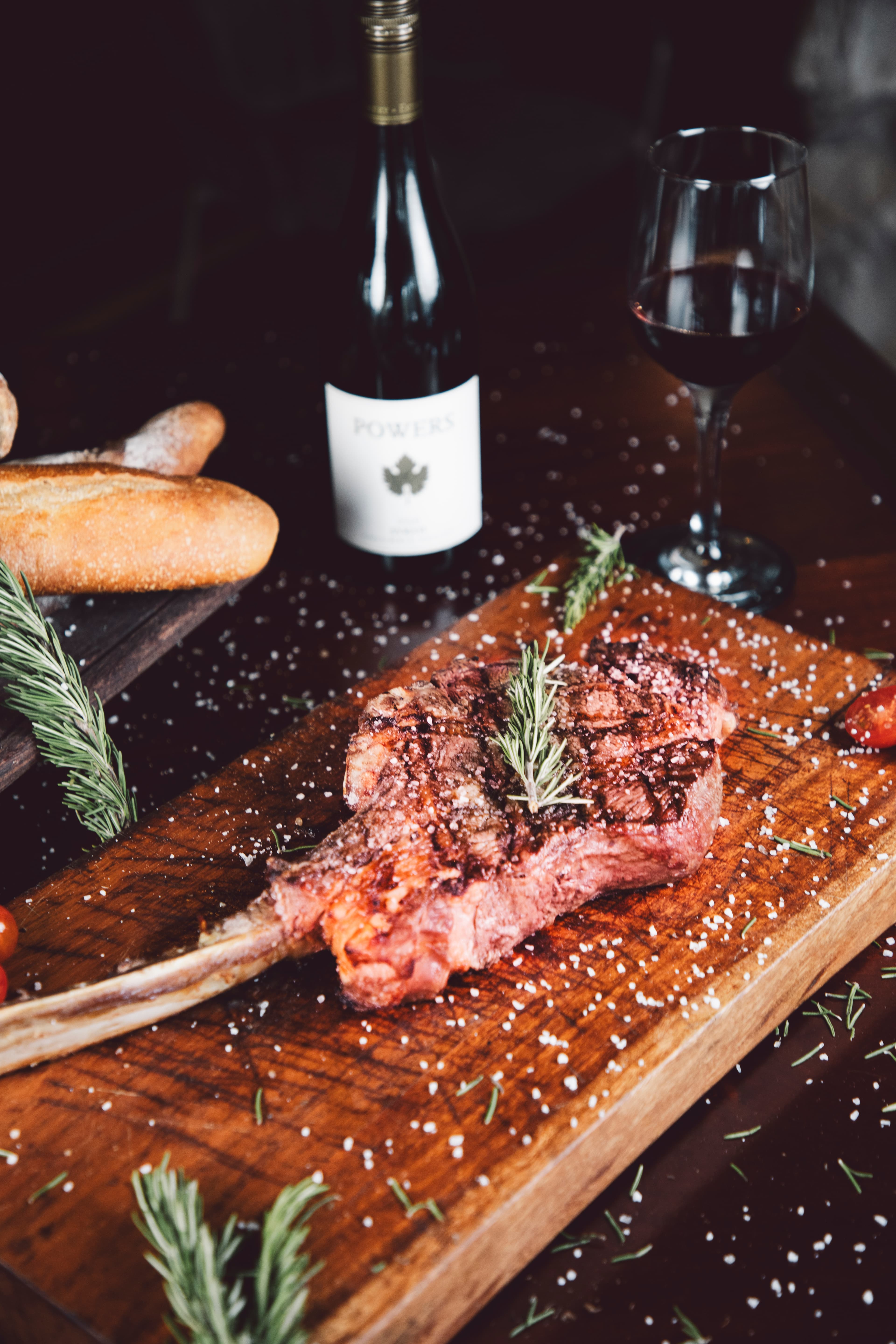 A beautifully presented steak garnished with rosemary, accompanied by a bottle of red wine and a glass, sits on a wooden board.