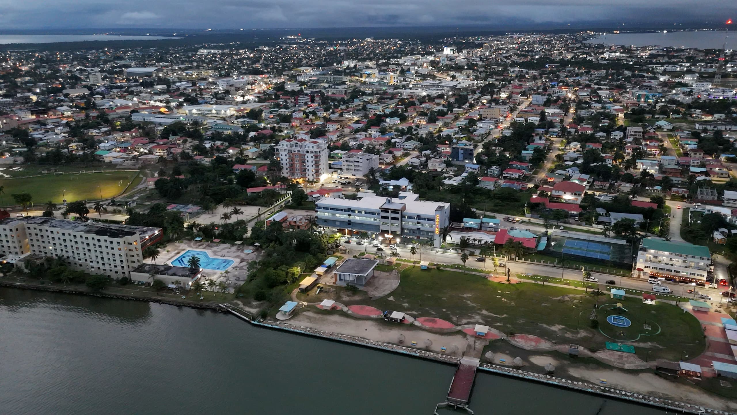 Aerial view of a coastal city at dusk, showcasing buildings, parks, and a waterfront.