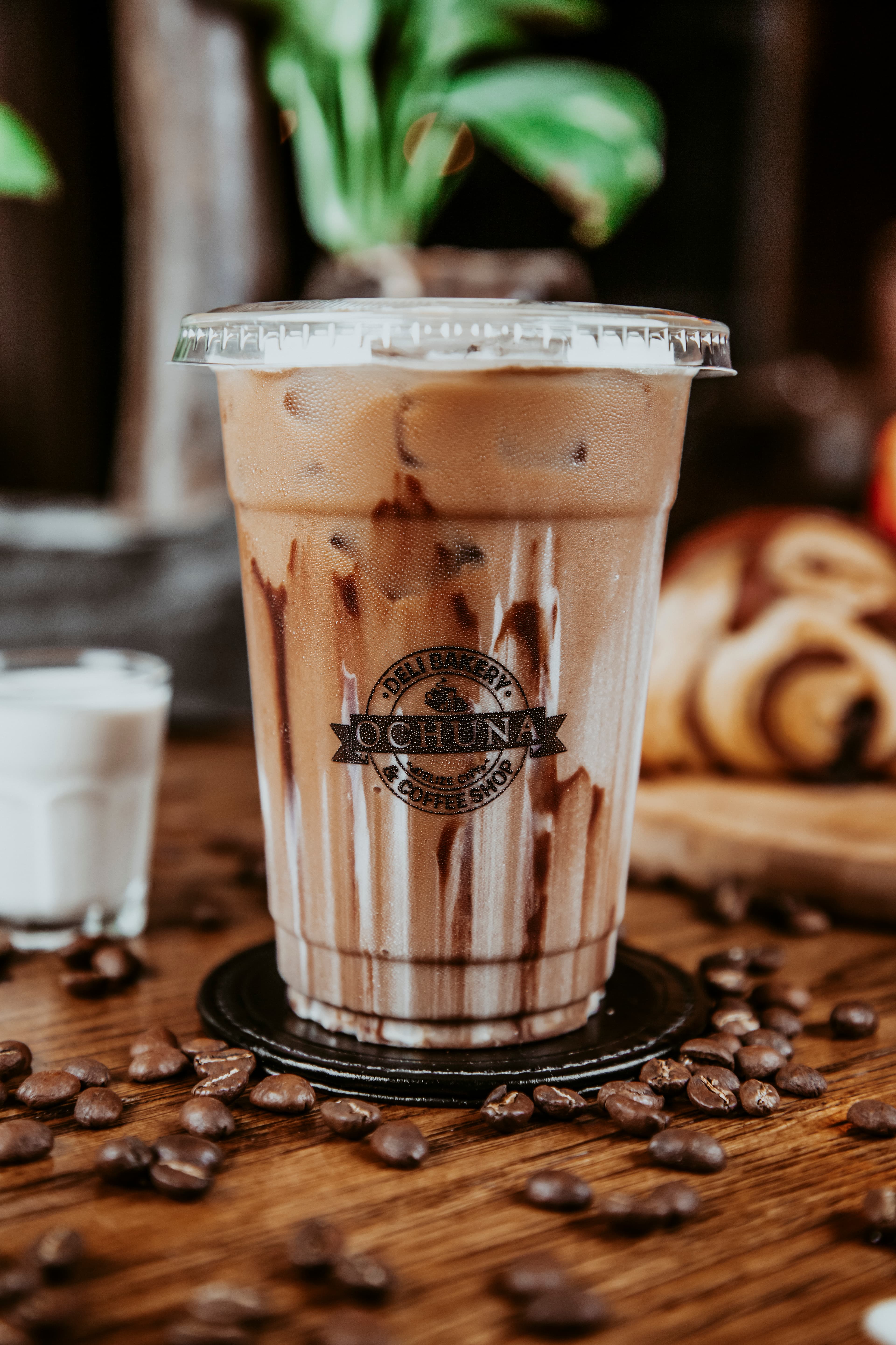 A chilled coffee drink with chocolate syrup in a clear cup, surrounded by coffee beans and a small glass of cream.