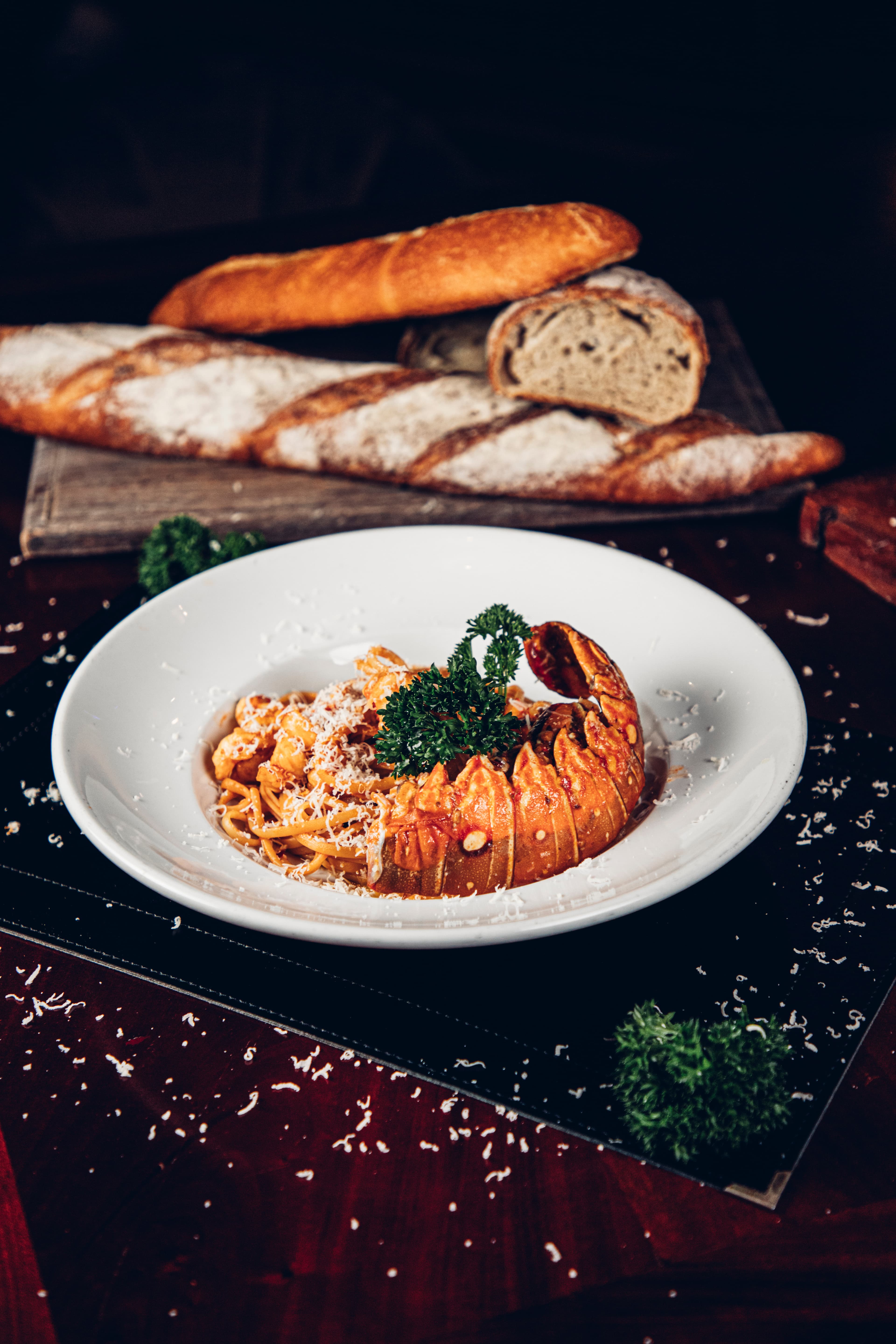 A plate of pasta topped with lobster and parsley, surrounded by grated cheese and fresh bread.