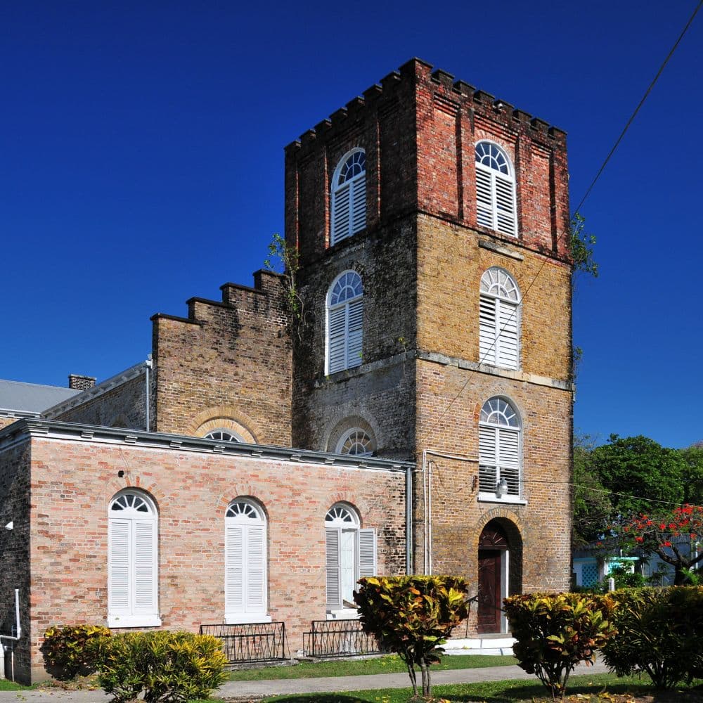 Historic brick building with a tall, cylindrical tower against a clear blue sky.